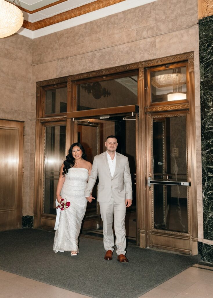 A couple holds hands as they walk into the waiting area  for their NYC City Hall elopement. 