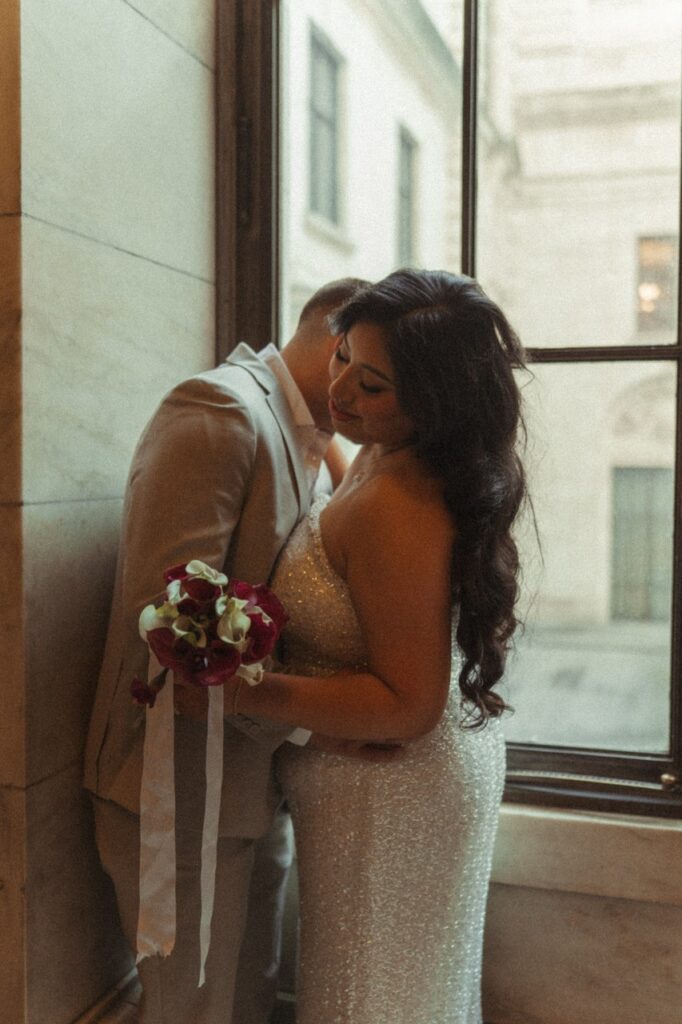 Newlyweds embrace near a window at NYC City Hall following their Manhattan elopement. 