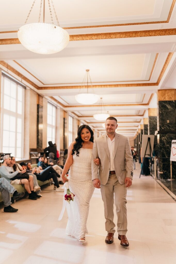 Newlyweds walk with arms linked through the halls of NYC City Hall following their Manhattan elopement.