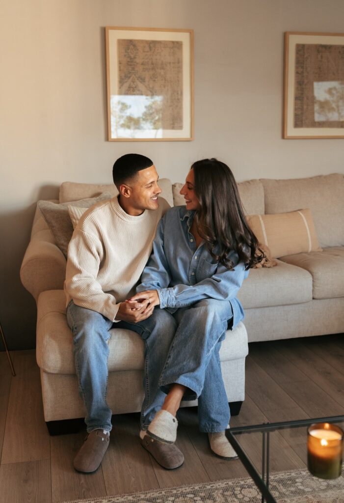 A newly engaged couple pose for a photo on their sofa in their Bronx apartment during in-home engagement pictures NYC> 