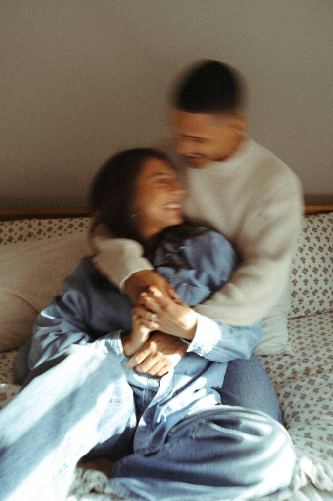 An editorial image of an engaged couple snuggling on their bed in their Bronx apartment during in-home engagement pictures NYC.