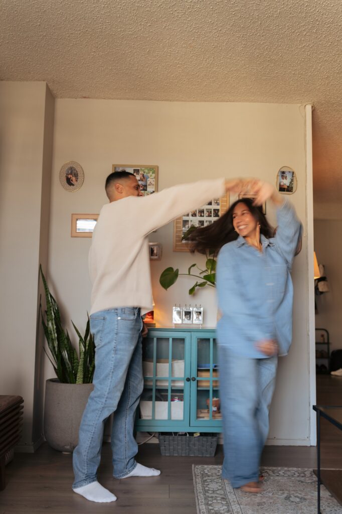 A young couple dance in their living room during in-home engagement pictures NYC. 