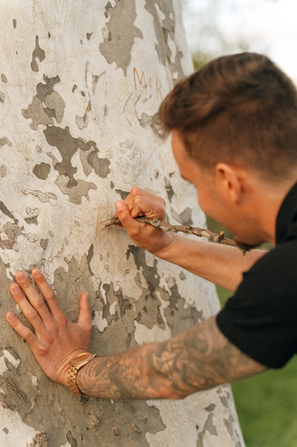A man carves an initial into the bark of a tree during new york engagement photography.