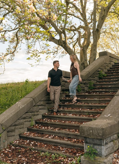 A couple holds hands as they walk down the stairs during an engagement session at Rockwood Hall State Park.