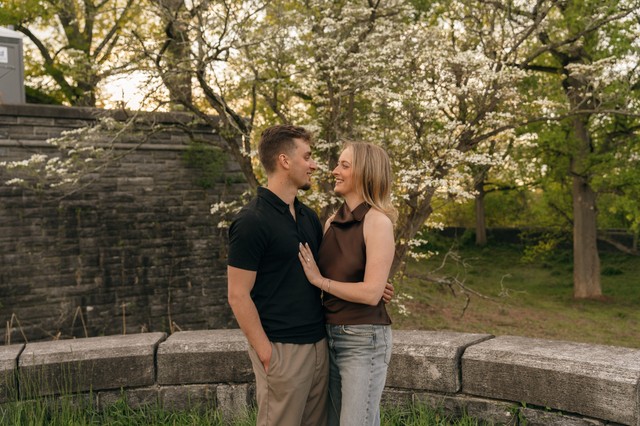 A newly engaged couple embrace next to a blooming tree at Rockwood Hall State Park.