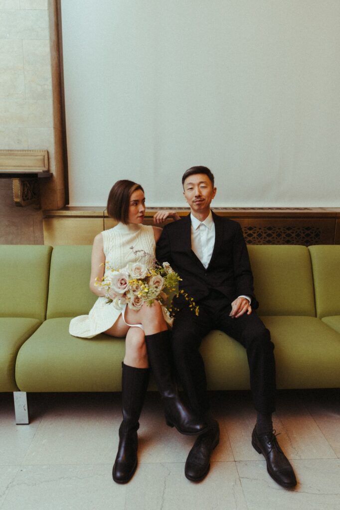 A couple awaiting their Manhattan City Hall marriage ceremony pose for an editorial photo on a green sofa. 